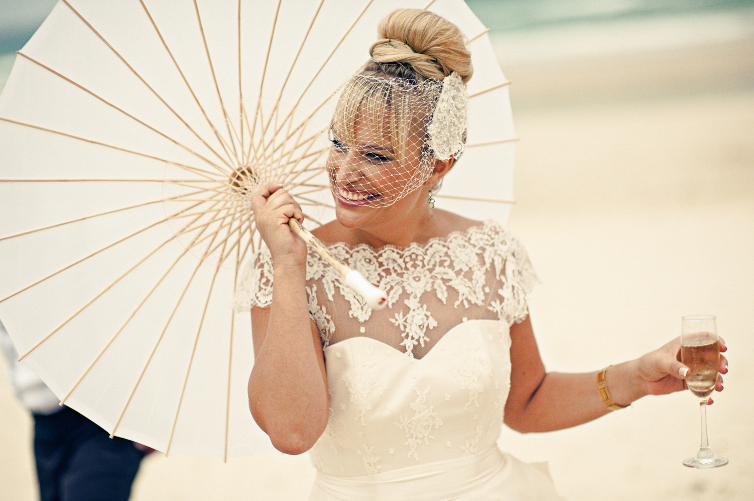 A beautiful bride standing on the beach holding an umbrella