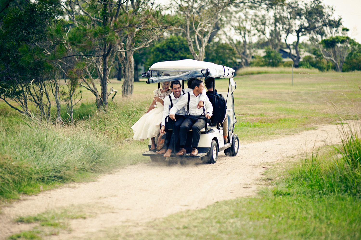 Bride and groom with their friends having fun in a golf cart on their wedding day